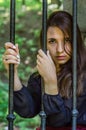 Young charming teenager girl with long dark hair sitting behind bars in a prison in the old castle fortress serving a sentence for Royalty Free Stock Photo