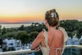 Young charming woman in a dress with a bare back stands on the balcony overlooking the sea at the sunset time Royalty Free Stock Photo