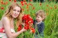 Young charming woman with long hair mom with her daughter walking on the field among the grass, wove a wreath, a bouquet of red po Royalty Free Stock Photo