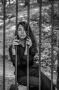 Young charming woman with long hair offender, sits behind bars in the old stone jail prisoner and looks pityingly through steel ba