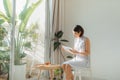 Young charming woman sitting on chair and reading book next to window at home Royalty Free Stock Photo