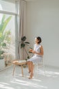 Young charming woman sitting on chair and reading book next to window at home Royalty Free Stock Photo