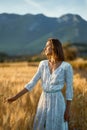 Young charming woman standing in golden field and looking away to sunset lights Royalty Free Stock Photo