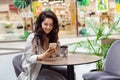 Young cheerfful woman using smartphone and drinking take away coffee in paper cup. Stylish woman sitting at cafe indoors Royalty Free Stock Photo