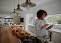 Young cheerful african american woman checking recipe on digital tablet while preparing vegetable salad in kitchen Royalty Free Stock Photo