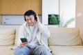asian guy listening to music in headphones sitting on sofa at home. A man alone on the couch feels good lifestyle. Royalty Free Stock Photo