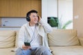 Cheerful asian guy listening to music in headphones sitting on sofa at home. A man alone on the couch feels good lifestyle. Royalty Free Stock Photo