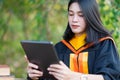 A young cheerful beautiful female gradute student wearing academic gown studying in college campus with books and lablet on table Royalty Free Stock Photo