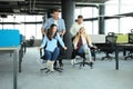 Young cheerful business people in smart casual wear having fun while racing on office chairs and smiling Royalty Free Stock Photo