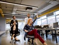 Young business people in smart casual wear having fun while racing on office chairs and smiling Royalty Free Stock Photo