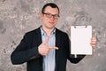 Young cheerful businessman or manager in glasses and suit holding clipboard with blank sheet of paper in his hands and Royalty Free Stock Photo