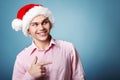 Young cheerful christmas man with santa`s hat point with hand le