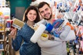 Young cheerful couple demonstrating tools for house renovating in paint store