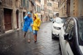 A young cheerful couple in raincoats is having fun while running from the rain towards the car during a walk the city. Walk, rain Royalty Free Stock Photo