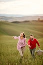 A young cheerful couple running on a large meadow while holding by hands. Love, relationship, together, nature Royalty Free Stock Photo