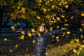 Young cheerful cute girl woman playing with fallen autumn yellow leaves in the park near the tree, laughing and smiling Royalty Free Stock Photo