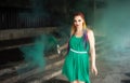 Cute girl in a green dress with African braids and colorful makeup posing with bright green smoke on the streets of a Royalty Free Stock Photo