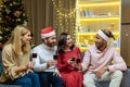 young cheerful group people, friends celebrate New Year countdown at home clink wine glasses while sitting on sofa at Royalty Free Stock Photo