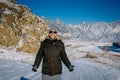 Young cheerful guy enjoying Christmas vacation in mountains. Attractive man laughs and gives thumbs up against snow-capped