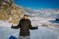 Young cheerful guy enjoying Christmas vacation in mountains. Attractive man laughs and gives thumbs up against snow-capped