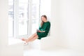 Young cheerful happy woman in dress holding mobile phone and smiling while sitting on windowsill