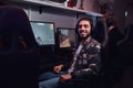 A young cheerful Indian guy wearing a military shirt sitting on a gamer chair and looking at a camera in a gaming club