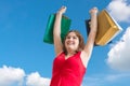 Young cheerful lady holds shopping bags in hands against blue sky