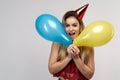 A young cheerful long-haired girl with a cap on her head and with balloons in her hands smiles happily opening her mouth. Royalty Free Stock Photo