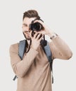 Young cheerful man photographer takes images with digital camera. Isolated on gray background. Studio shot. Royalty Free Stock Photo