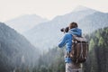 Young cheerful man photographer taking photographs with digital camera in a mountains.