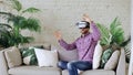 Young cheerful man wearing virtual reality headset having 360 VR video experience while sitting on couch in living room Royalty Free Stock Photo