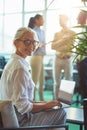 Young cheerful mature business woman sitting in the modern office and using laptop, smiling at camera while her Royalty Free Stock Photo