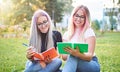 Young cheerful millennial university student girls sitting in the grass on the campus and learning from their booklets - Friends Royalty Free Stock Photo