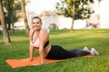 Young cheerful plus size woman in sporty top and leggings practicing yoga on orange yoga mat joyfully looking in camera