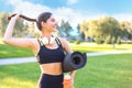 Young cheerful sports woman walking in urban park holding fitness rug. Royalty Free Stock Photo