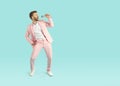 Young cheerful stylish man in pink suit singing song in the microphone isolated on blue background. Royalty Free Stock Photo