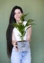 Young cheerful woman in casual clothes standing with pleased smile and holding flowerpot with houseplant