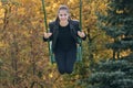 Young cheerful woman goes for a drive on swing on autumn park background