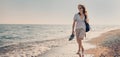 Young cheerful woman in a hat and sunglasses walking on the seashore with a backpack at sunset. Summer sea holidays Royalty Free Stock Photo