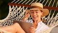 Young cheerful woman in straw hat using digital tablet, having video call while relaxing in the hammock on tropical beach on hot Royalty Free Stock Photo