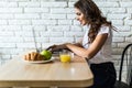 Young cheerful woman using on laptop computer and eating fruits in the kitchen in the morning Royalty Free Stock Photo