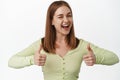 Young cheerful woman winking and showing her support with thumbs up, smiling give confidence boost, praising nice work Royalty Free Stock Photo