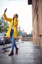 A young cheerful woman in a yellow raincoat is listening to the music while walking the city on a rainy day. Walk, rain, city Royalty Free Stock Photo