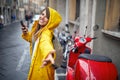 A young cheerful woman in a yellow raincoat is posing for a photo while walking the city on a rainy day and listening to the music Royalty Free Stock Photo