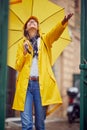 A young cheerful woman with a yellow raincoat and umbrella who is enjoying the rain while walking the city on a cloudy day. Walk, Royalty Free Stock Photo