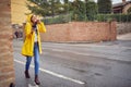 A young cheerful woman in a yellow raincoat who is in a good mood while walking the city on a rainy day and listening to the music Royalty Free Stock Photo