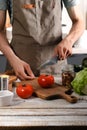 A young chef in a brown apron uses a kitchen knife to cut vegetables for a delicious salad. Cooking delicious and healthy food in Royalty Free Stock Photo
