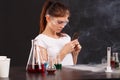 A young chemist girl, uses a black smartphone. The concept of science. On a dark background.