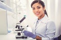 Young chemist wearing white uniform sitting near microscope