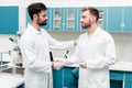 Young chemists in white coats shaking hands in scientific laboratory
